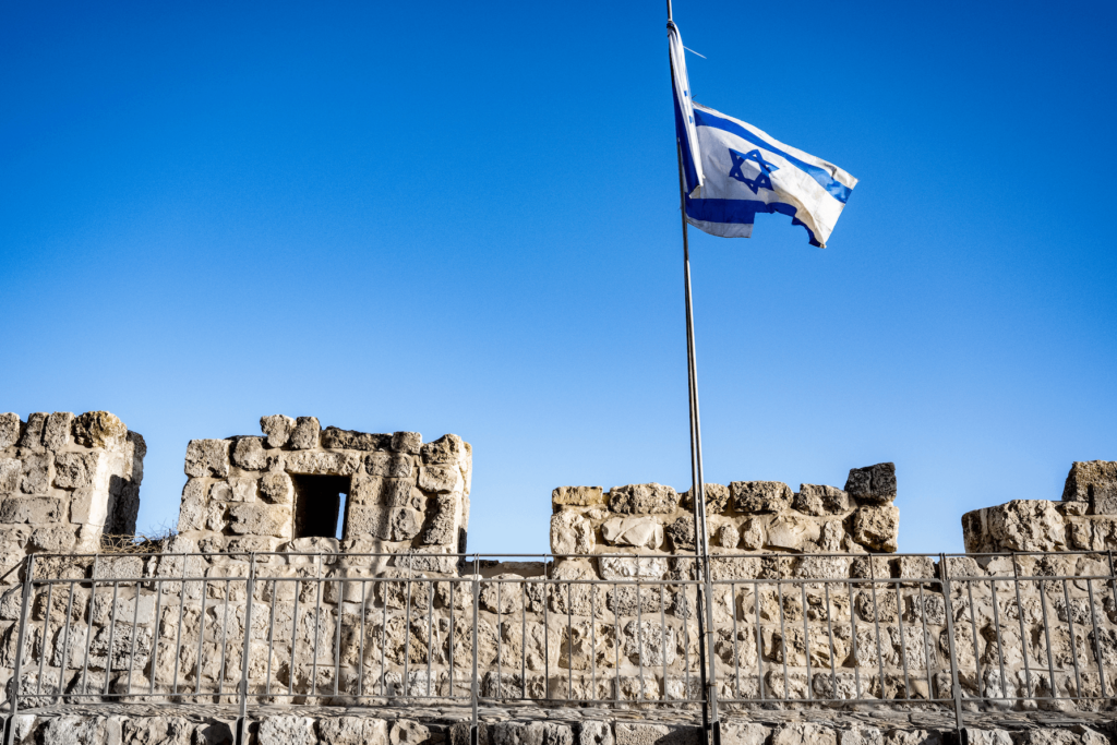 Israeli flag flies blue sky above ruins